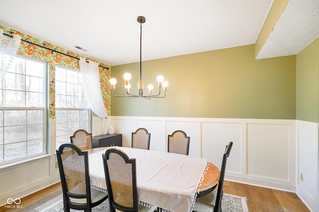 dining space featuring a chandelier, visible vents, wainscoting, and wood finished floors