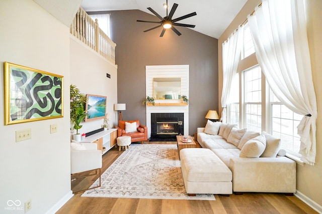 living area featuring a ceiling fan, high vaulted ceiling, wood finished floors, and a tile fireplace