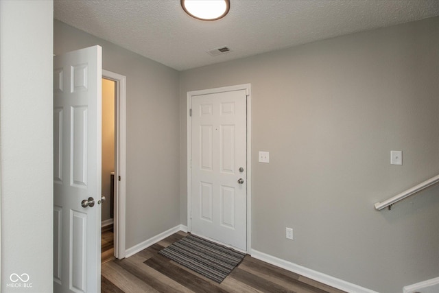 entryway featuring a textured ceiling, wood finished floors, visible vents, and baseboards