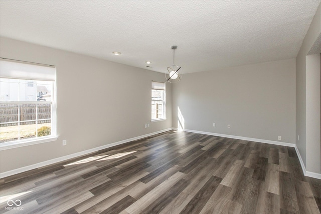 empty room with a textured ceiling, dark wood-type flooring, and baseboards