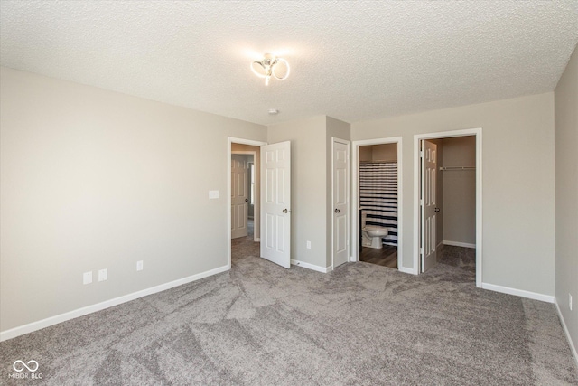 unfurnished bedroom with a spacious closet, carpet, baseboards, and a textured ceiling