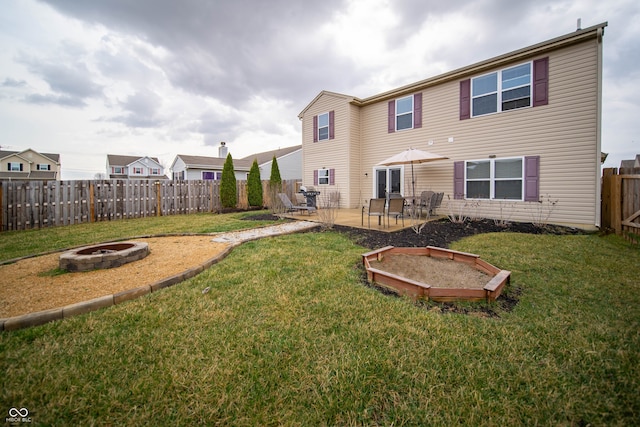 rear view of property featuring a yard, a fire pit, a fenced backyard, and a patio area