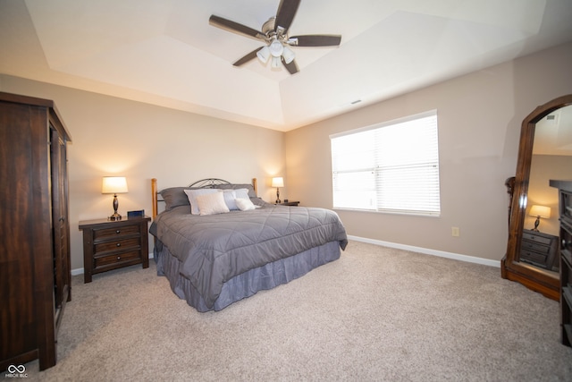 bedroom with ceiling fan, baseboards, a tray ceiling, light carpet, and arched walkways