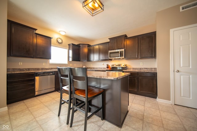 kitchen featuring a breakfast bar area, visible vents, a kitchen island, dark brown cabinetry, and appliances with stainless steel finishes