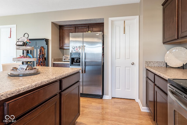 kitchen featuring light countertops, light wood finished floors, appliances with stainless steel finishes, and dark brown cabinets