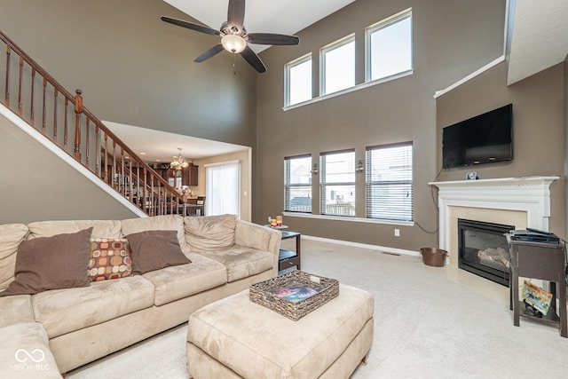 living room with carpet, baseboards, a fireplace with flush hearth, stairs, and ceiling fan with notable chandelier