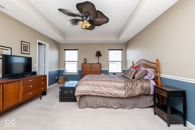 bedroom with a raised ceiling, light colored carpet, baseboards, and ceiling fan