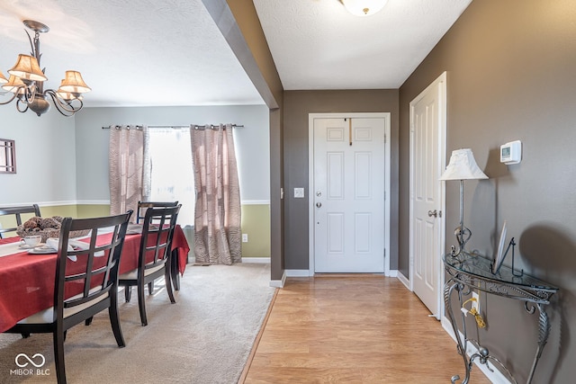 foyer entrance with light wood-style floors, baseboards, a notable chandelier, and a textured ceiling