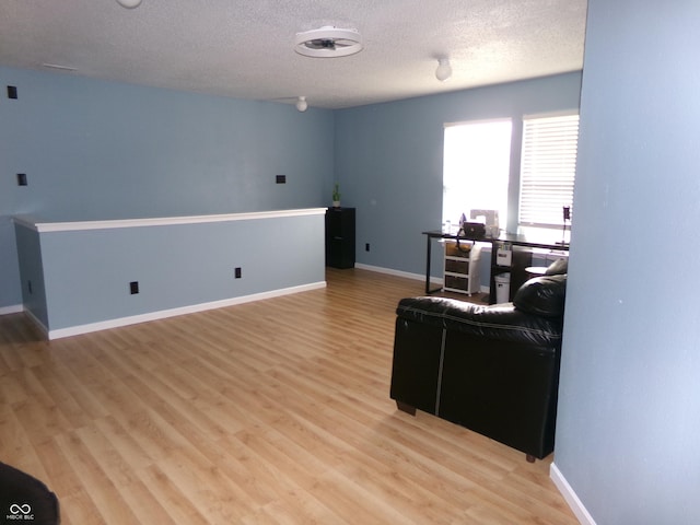 living area featuring baseboards, a textured ceiling, and light wood finished floors