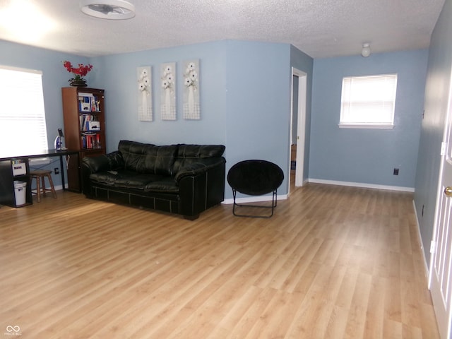 living area with light wood-type flooring, baseboards, and a textured ceiling