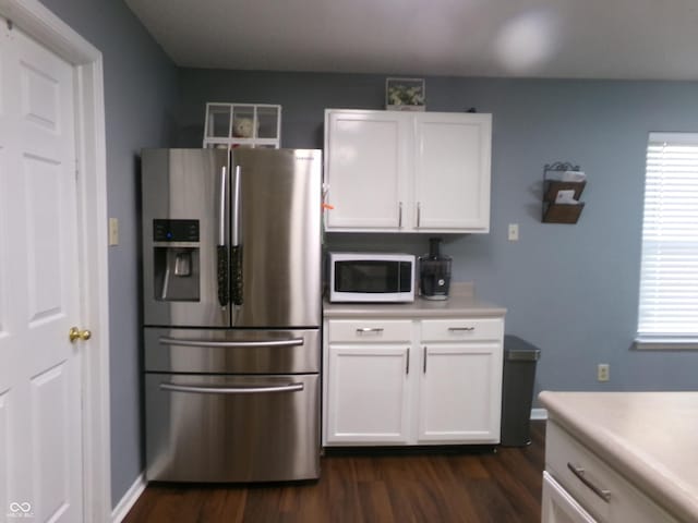 kitchen with white microwave, dark wood-type flooring, light countertops, stainless steel refrigerator with ice dispenser, and white cabinets