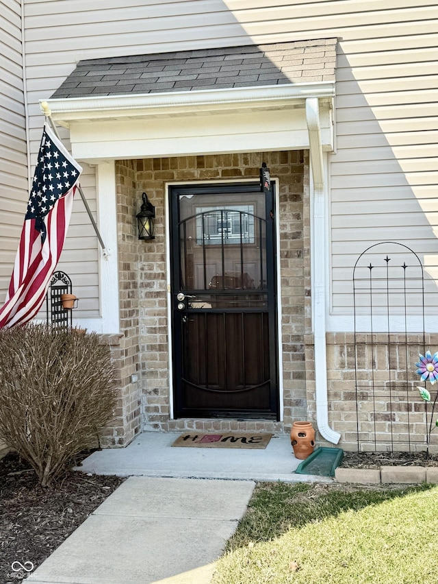 doorway to property featuring brick siding and a shingled roof