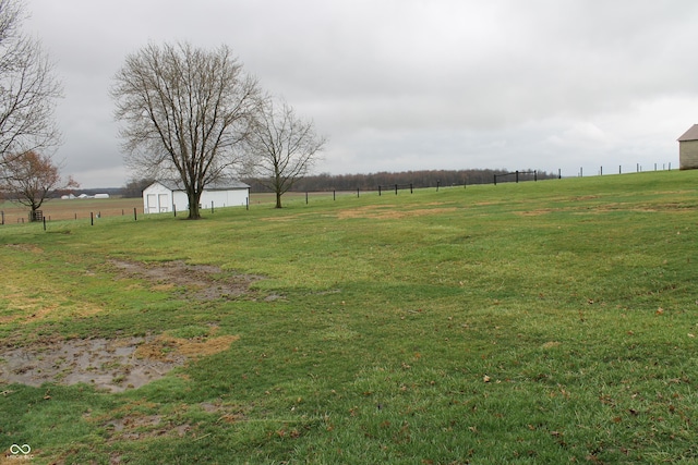 view of yard featuring a rural view, an outdoor structure, and fence