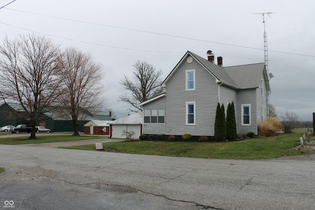 view of home's exterior featuring a lawn, a chimney, an outdoor structure, and metal roof