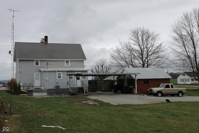 rear view of house with an attached carport, driveway, a chimney, a lawn, and metal roof