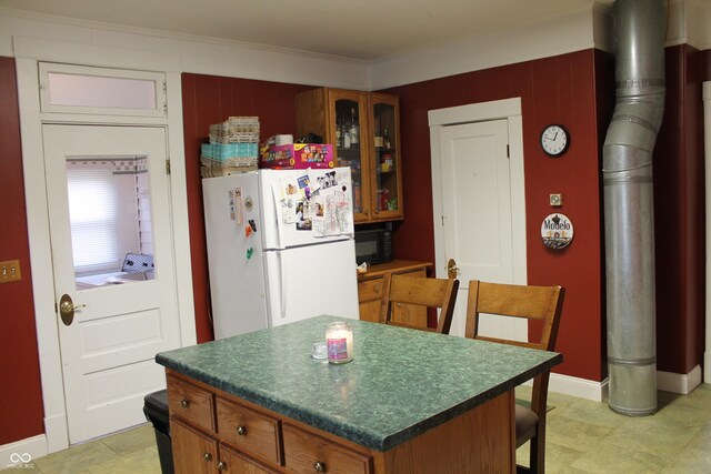 kitchen featuring dark countertops, a center island, glass insert cabinets, brown cabinets, and freestanding refrigerator