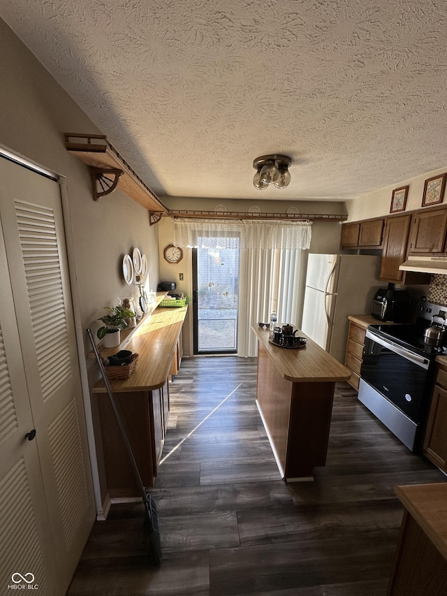 kitchen featuring dark wood-type flooring, butcher block countertops, under cabinet range hood, freestanding refrigerator, and stainless steel electric range oven