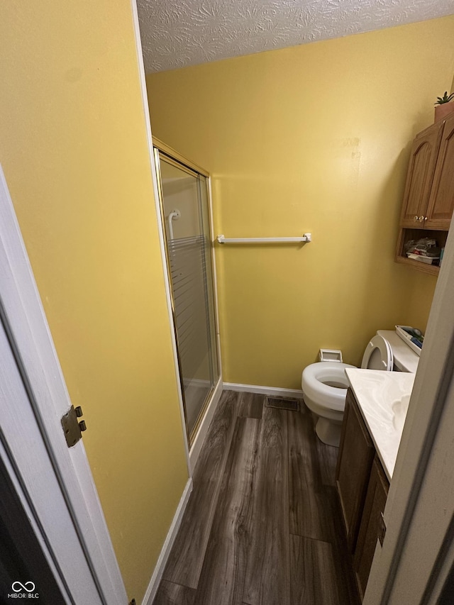 full bathroom featuring a shower stall, toilet, vanity, wood finished floors, and a textured ceiling