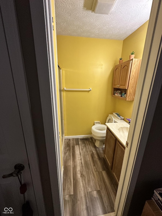bathroom featuring vanity, toilet, wood finished floors, and a textured ceiling