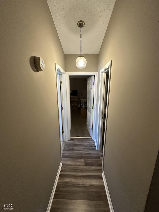 corridor featuring dark wood-style floors, a textured ceiling, and baseboards