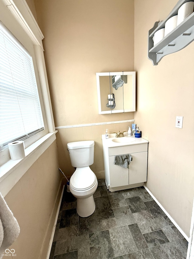 bathroom featuring stone finish floor, toilet, vanity, and baseboards