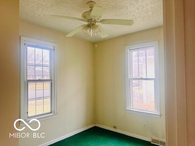unfurnished room with visible vents, a textured ceiling, plenty of natural light, and dark colored carpet