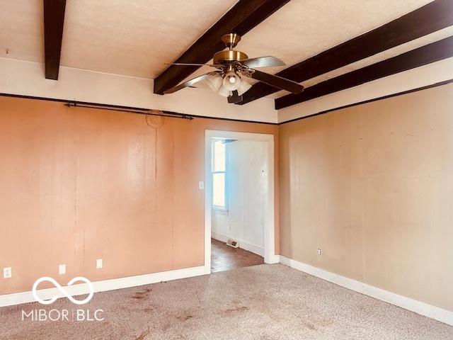 unfurnished room featuring carpet, baseboards, ceiling fan, and beamed ceiling