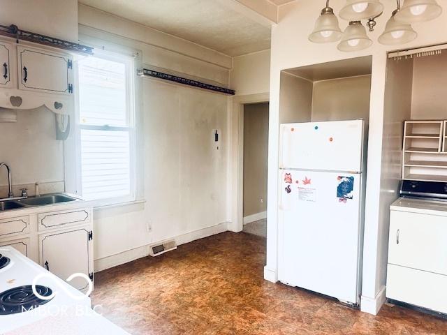 kitchen with a sink, light countertops, freestanding refrigerator, washer / dryer, and visible vents