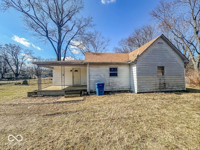 rear view of property featuring covered porch, a lawn, and a shingled roof