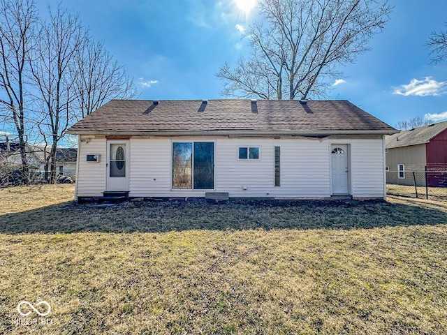 rear view of house with a lawn, a shingled roof, and fence