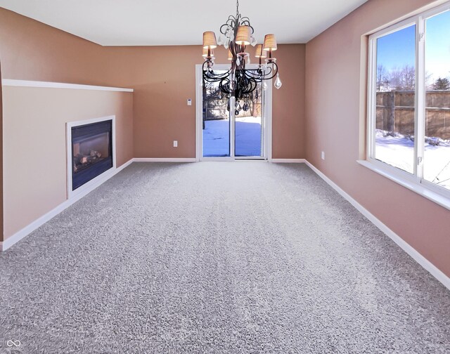 unfurnished dining area with a glass covered fireplace, an inviting chandelier, baseboards, and carpet floors