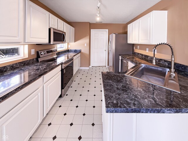 kitchen with a sink, stainless steel appliances, dark countertops, and white cabinets