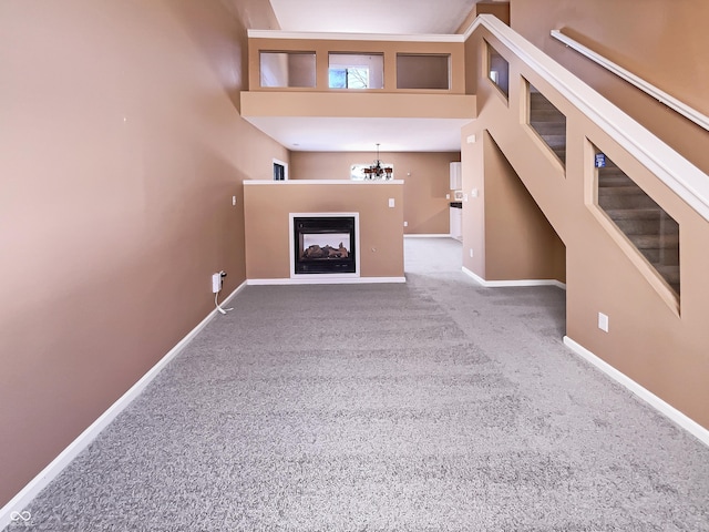 unfurnished living room featuring a multi sided fireplace, baseboards, carpet, and a chandelier