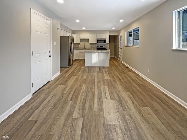 kitchen with white cabinets, stainless steel appliances, wood finished floors, a sink, and baseboards