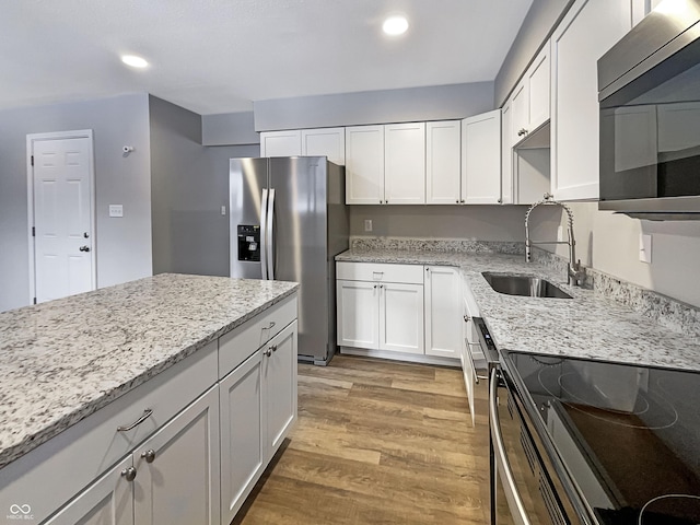 kitchen with light stone counters, a sink, light wood-type flooring, white cabinetry, and appliances with stainless steel finishes
