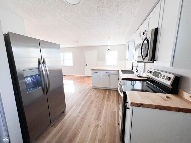 kitchen featuring light wood finished floors, a peninsula, a textured ceiling, stainless steel appliances, and wood counters