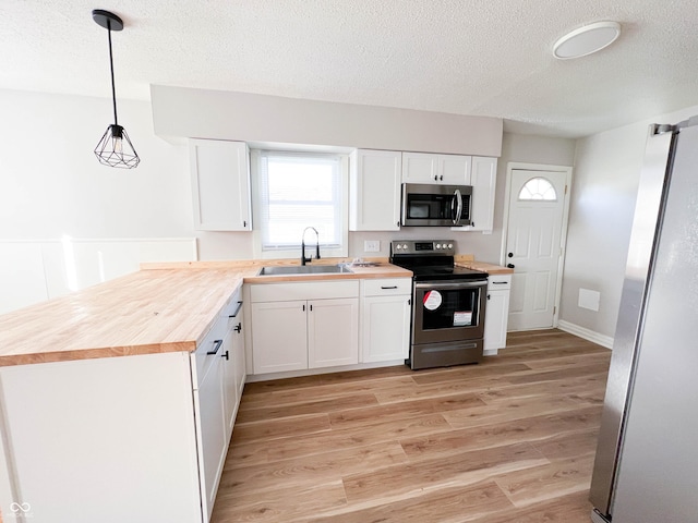 kitchen featuring light wood-style flooring, a sink, wood counters, white cabinetry, and stainless steel appliances