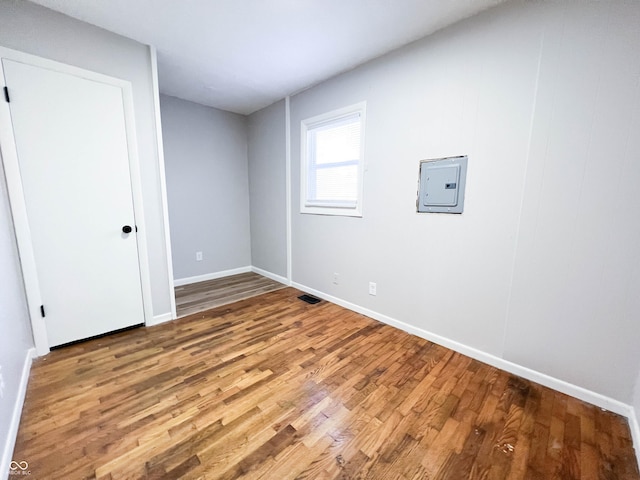 spare room featuring electric panel, visible vents, baseboards, and wood finished floors