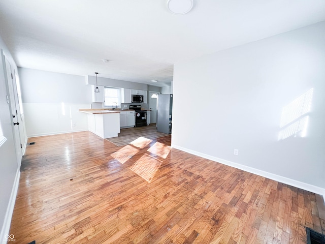 unfurnished living room featuring light wood finished floors, visible vents, baseboards, and a sink