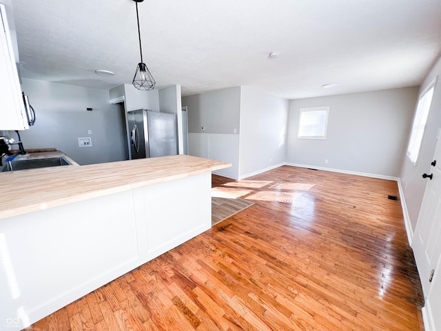 kitchen featuring light wood-type flooring, a peninsula, freestanding refrigerator, white cabinets, and a sink