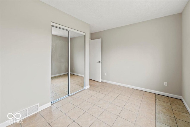 unfurnished bedroom with visible vents, baseboards, light tile patterned floors, a closet, and a textured ceiling
