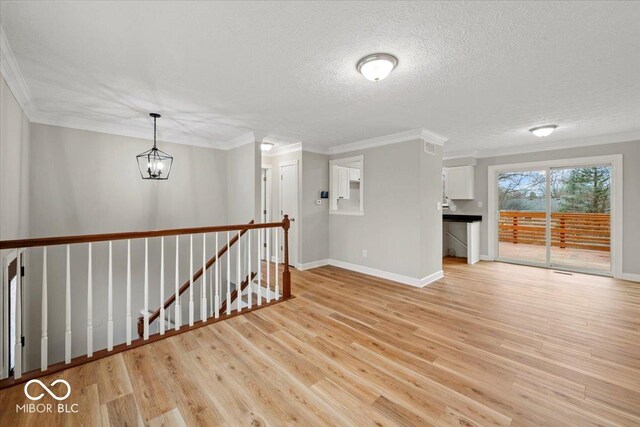 spare room featuring crown molding, baseboards, light wood-type flooring, a notable chandelier, and a textured ceiling