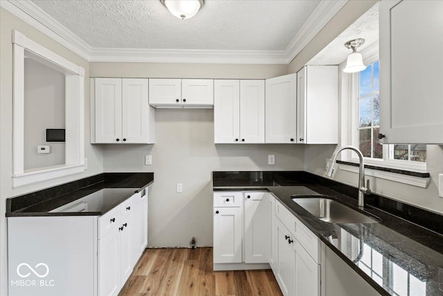 kitchen with a sink, a textured ceiling, dark stone counters, light wood-style floors, and white cabinets