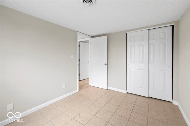 unfurnished bedroom featuring visible vents, a textured ceiling, a closet, light tile patterned floors, and baseboards