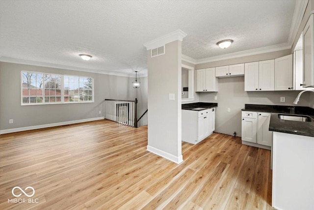 kitchen featuring dark countertops, visible vents, light wood finished floors, ornamental molding, and a sink