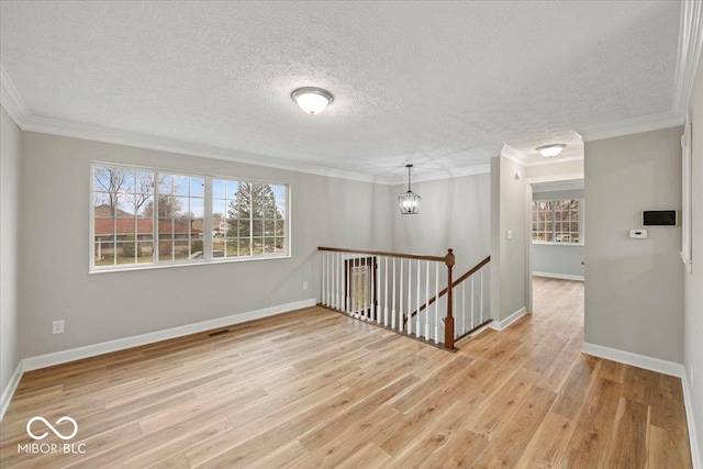 spare room with light wood finished floors, baseboards, a chandelier, ornamental molding, and a textured ceiling