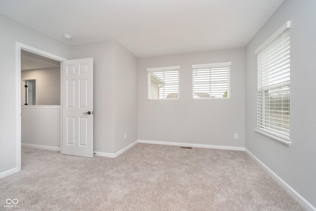 empty room featuring baseboards, visible vents, and light colored carpet