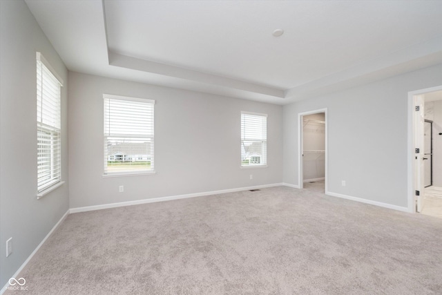 interior space with baseboards, a walk in closet, carpet flooring, and a raised ceiling