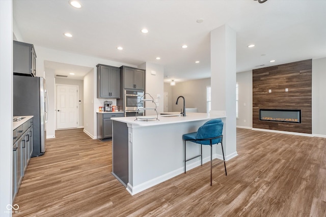 kitchen with a kitchen bar, light wood-type flooring, gray cabinets, a sink, and appliances with stainless steel finishes