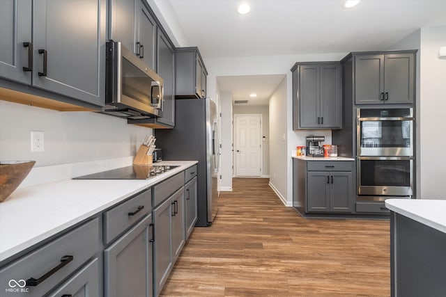 kitchen featuring light countertops, light wood finished floors, stainless steel appliances, recessed lighting, and gray cabinetry